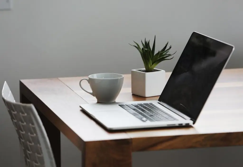 On a kitchen table, a notebook, a bowl of breakfast and a laptop mid video call